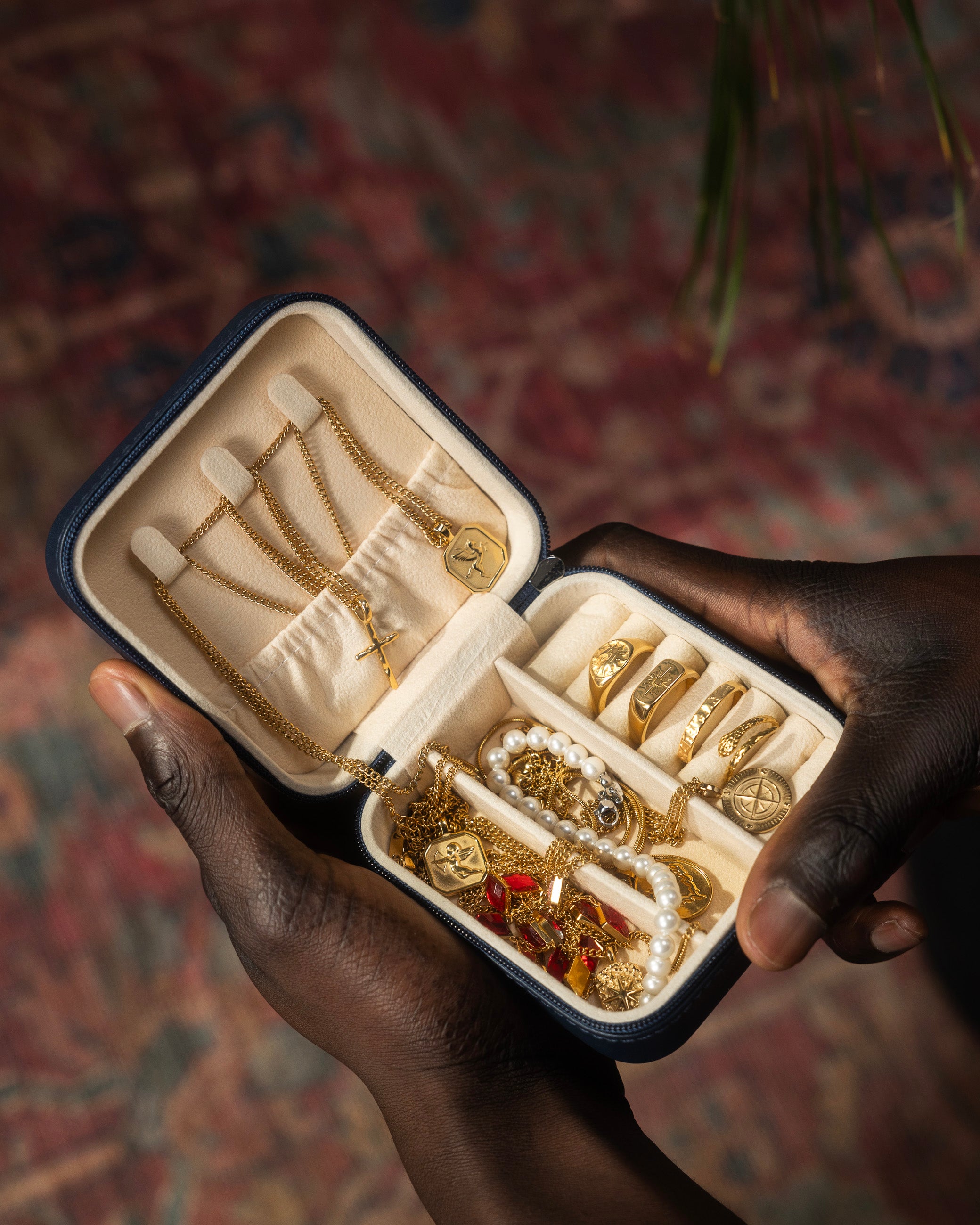 Open navy zip jewelry case with beige interior displaying gold chains and pendants.