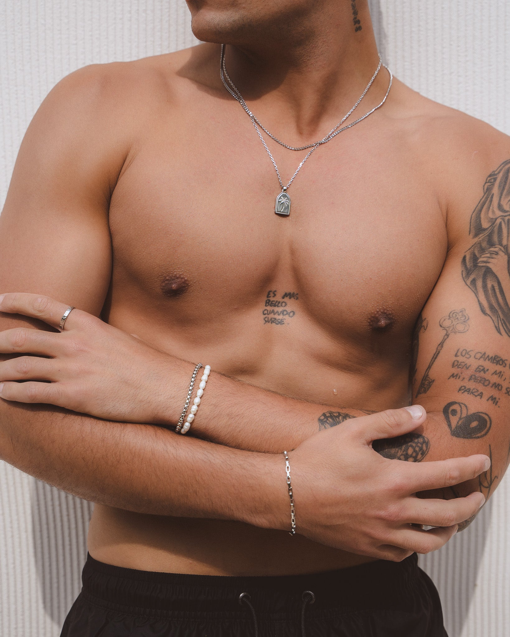 Man wearing layered silver chains with a palm tree pendant resting on his chest.