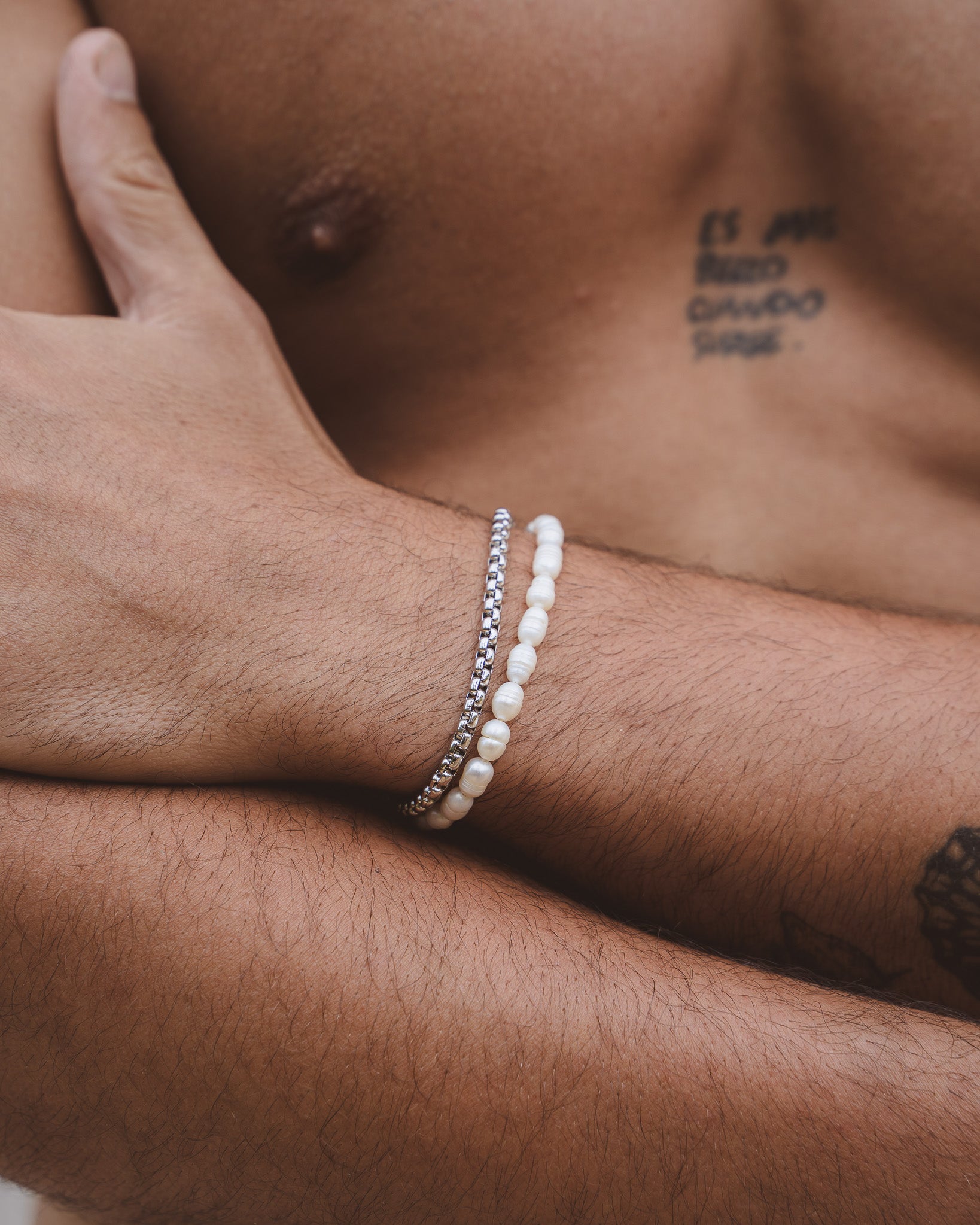 Close up of wrist with NOIR silver bracelet and white beaded bracelet forearm tattoo visible