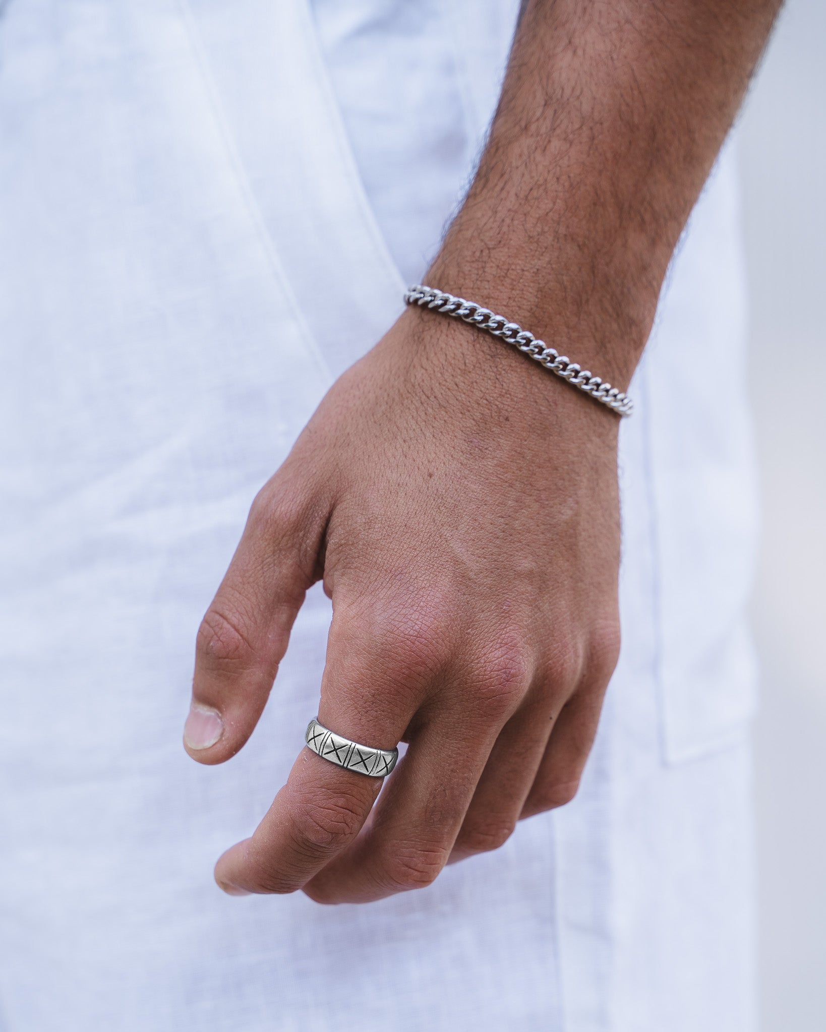 Silver curb chain bracelet on a wrist with a textured silver ring visible at the edge