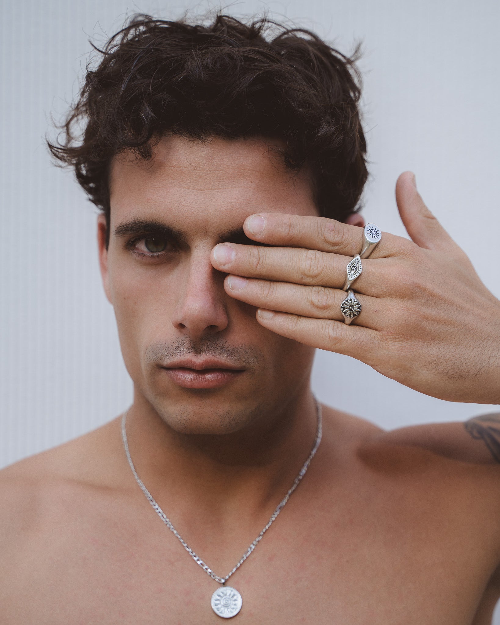 Close up of a man’s hand displaying ENERGY SILVER RING stacks with sun, eye, and floral motifs on silver bands.