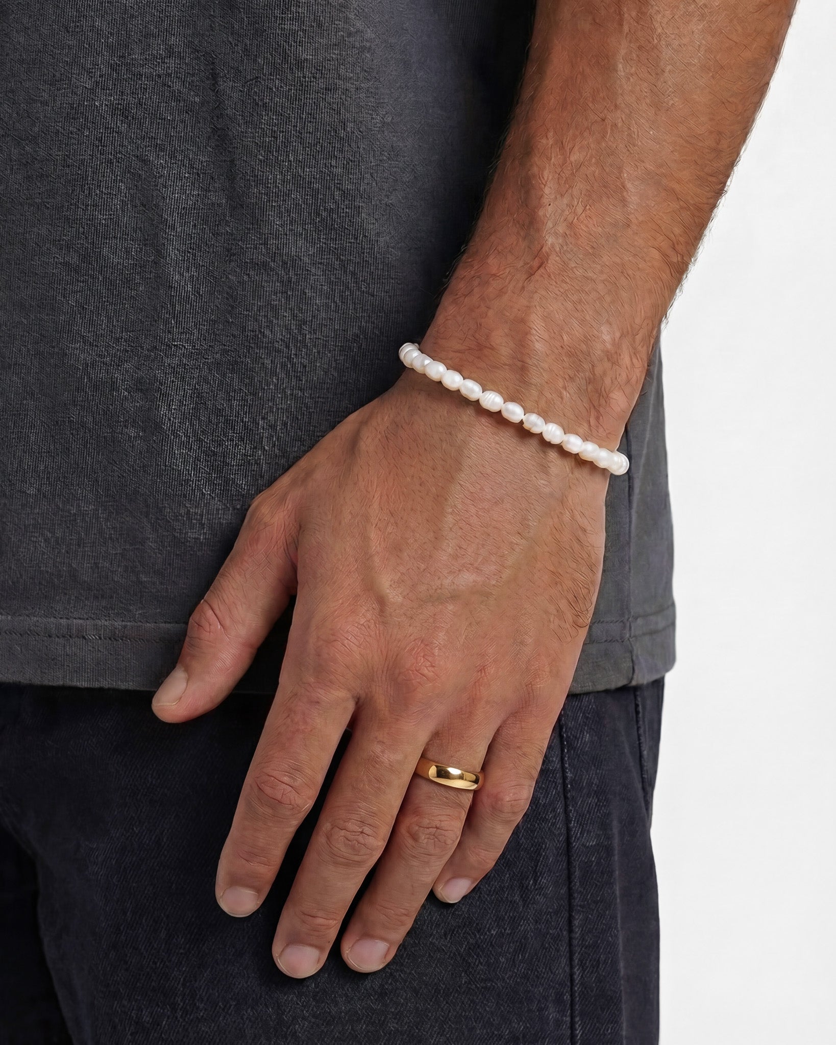 Man wearing a gold band ring and a white pearl bracelet on the wrist