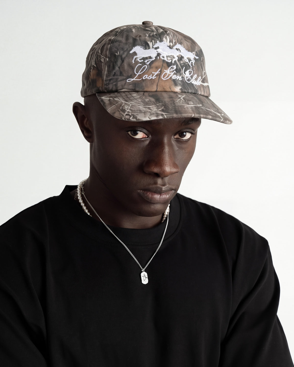 Camo baseball cap with white embroidered horses and Last Gen Club text on a model against a light background