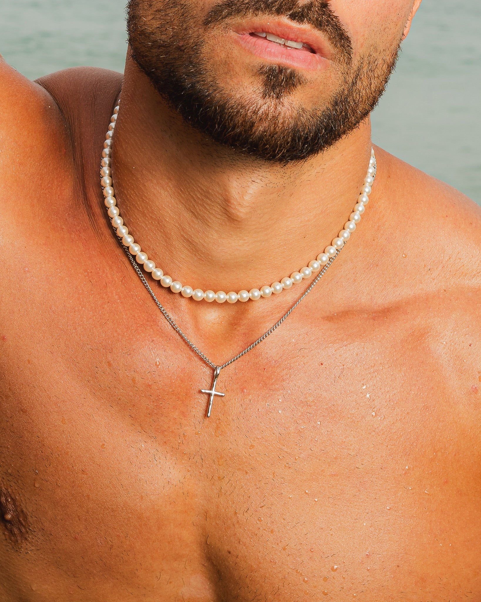 Collar de plata con cruz superpuesto a una hilera de perlas sobre el pecho.