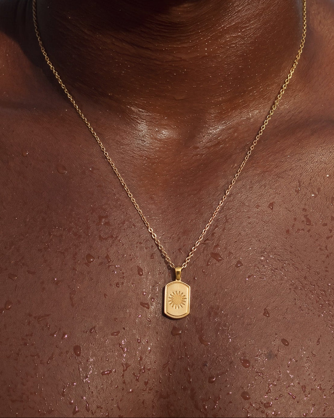 DAYSTAR gold necklace worn on dark skin with a rectangular sunburst pendant