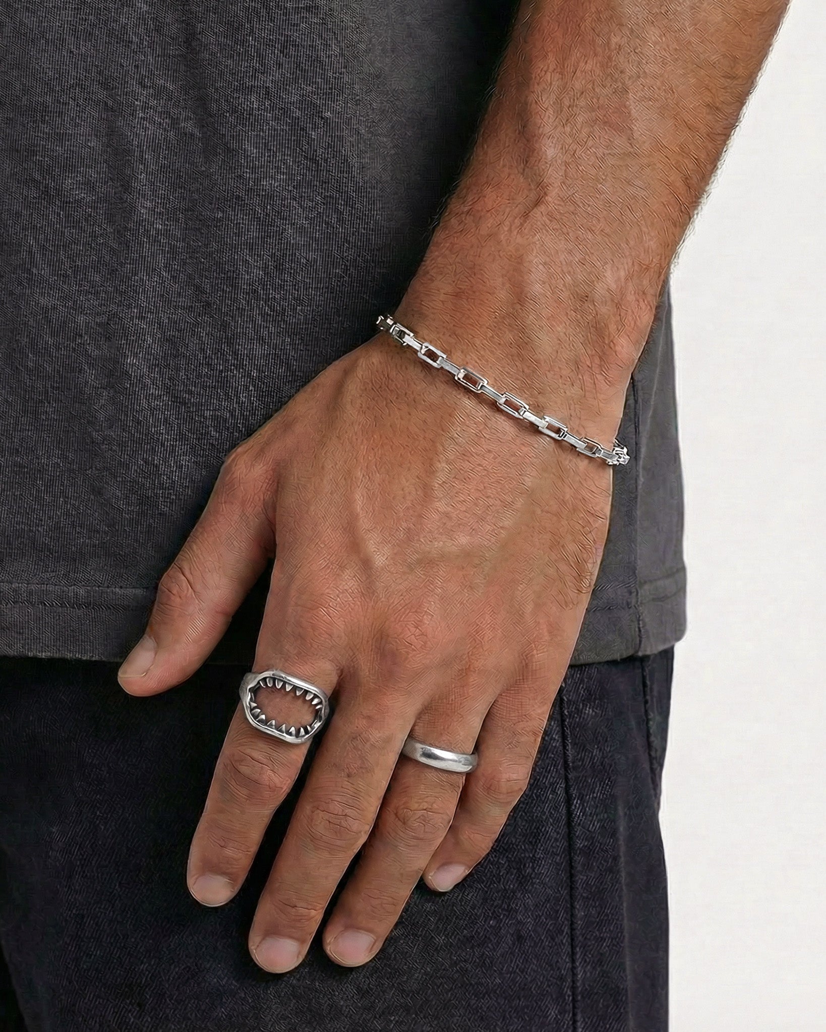 Silver rectangular link bracelet worn on a man's wrist against dark clothing.