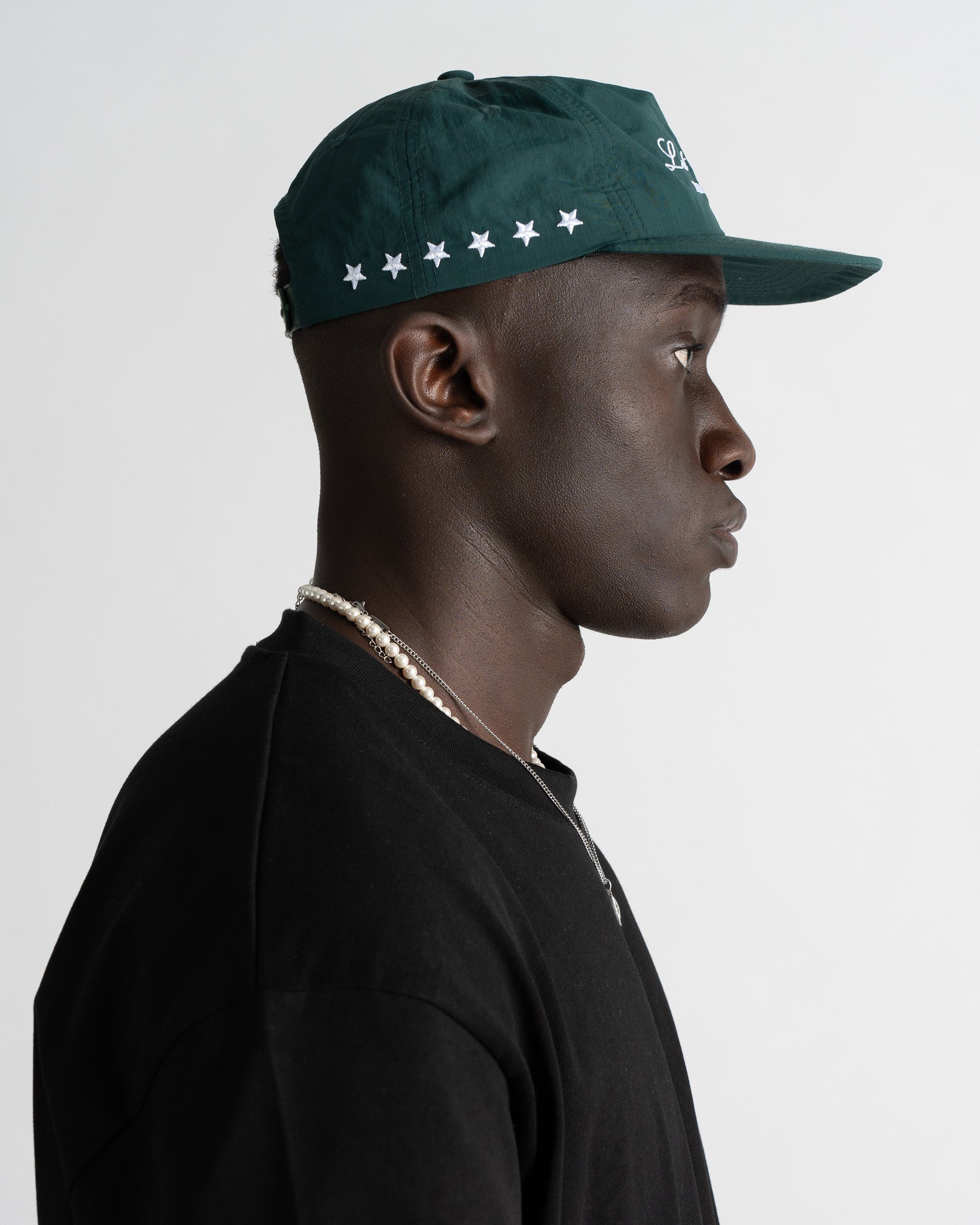 Perfil de gorra verde de nailon de cinco paneles en un modelo con bordado de estrellas blancas en el panel trasero.