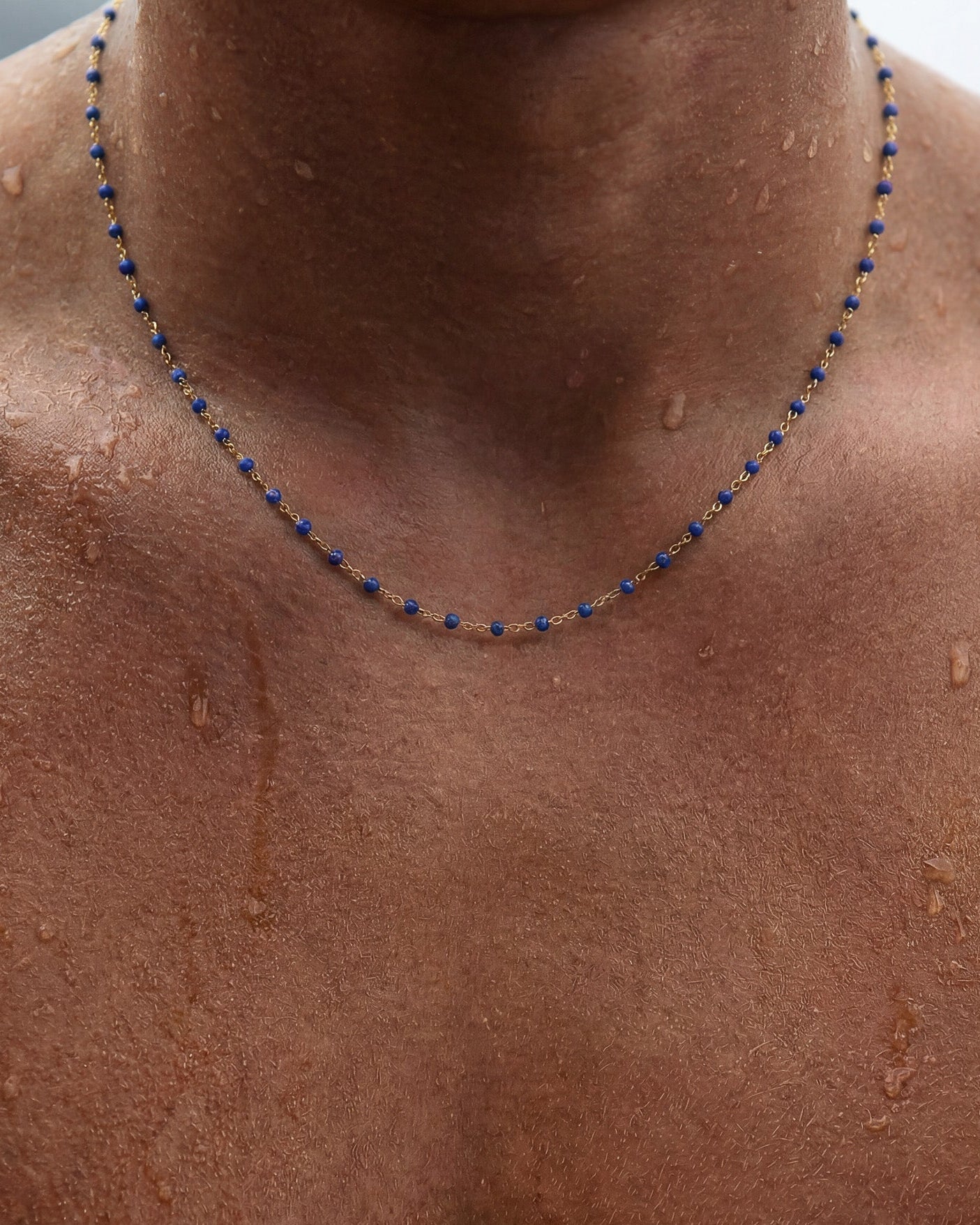 GEM GOLD CHAIN necklace with blue beads along a gold chain draped around the neck on wet skin