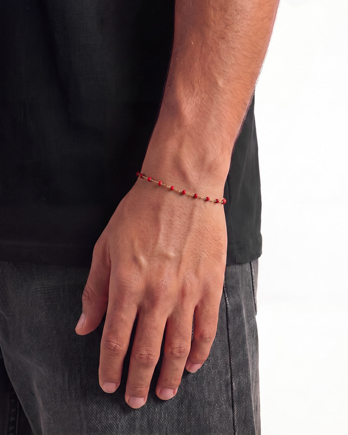 Vista lateral de una pulsera dorada con cuentas rojas en la muñeca