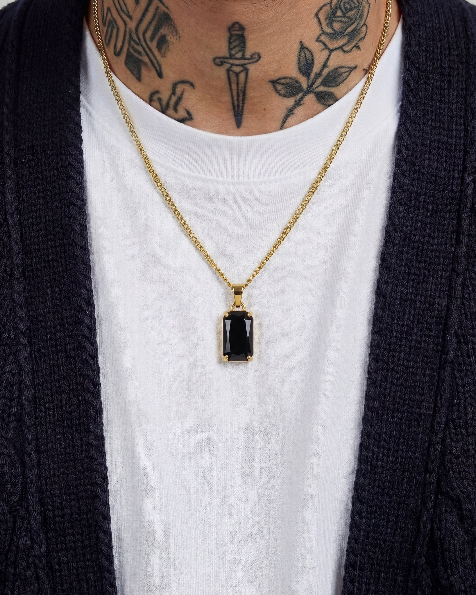 VOLT GOLD NECKLACE with a rectangular black gemstone pendant resting on a white T shirt under a dark cardigan