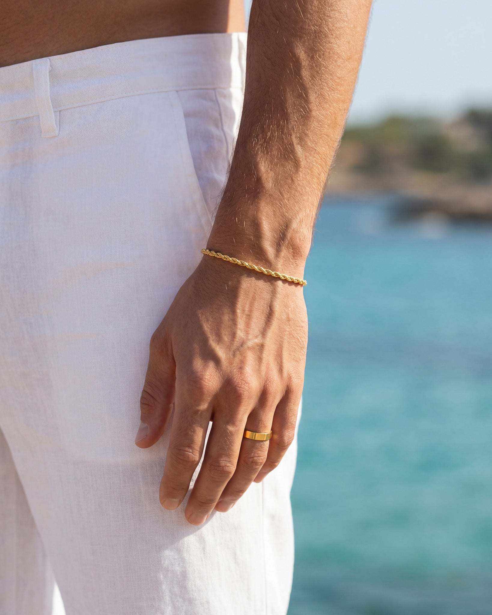 Close up of a gold chain bracelet on the wrist with a gold ring on the finger