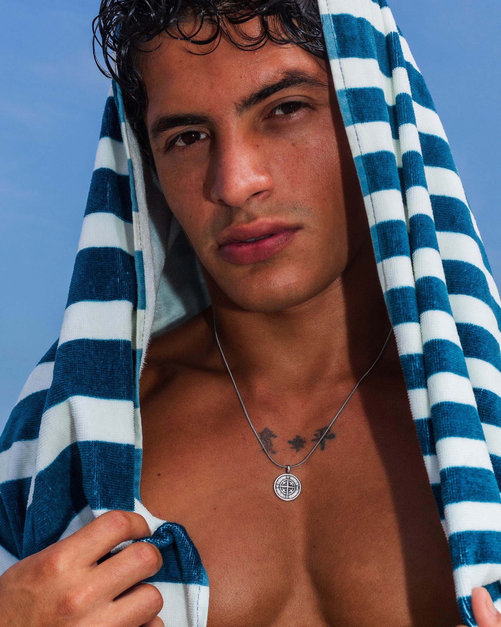 Mojave silver necklace worn by a man with a blue striped towel; compass pendant visible.