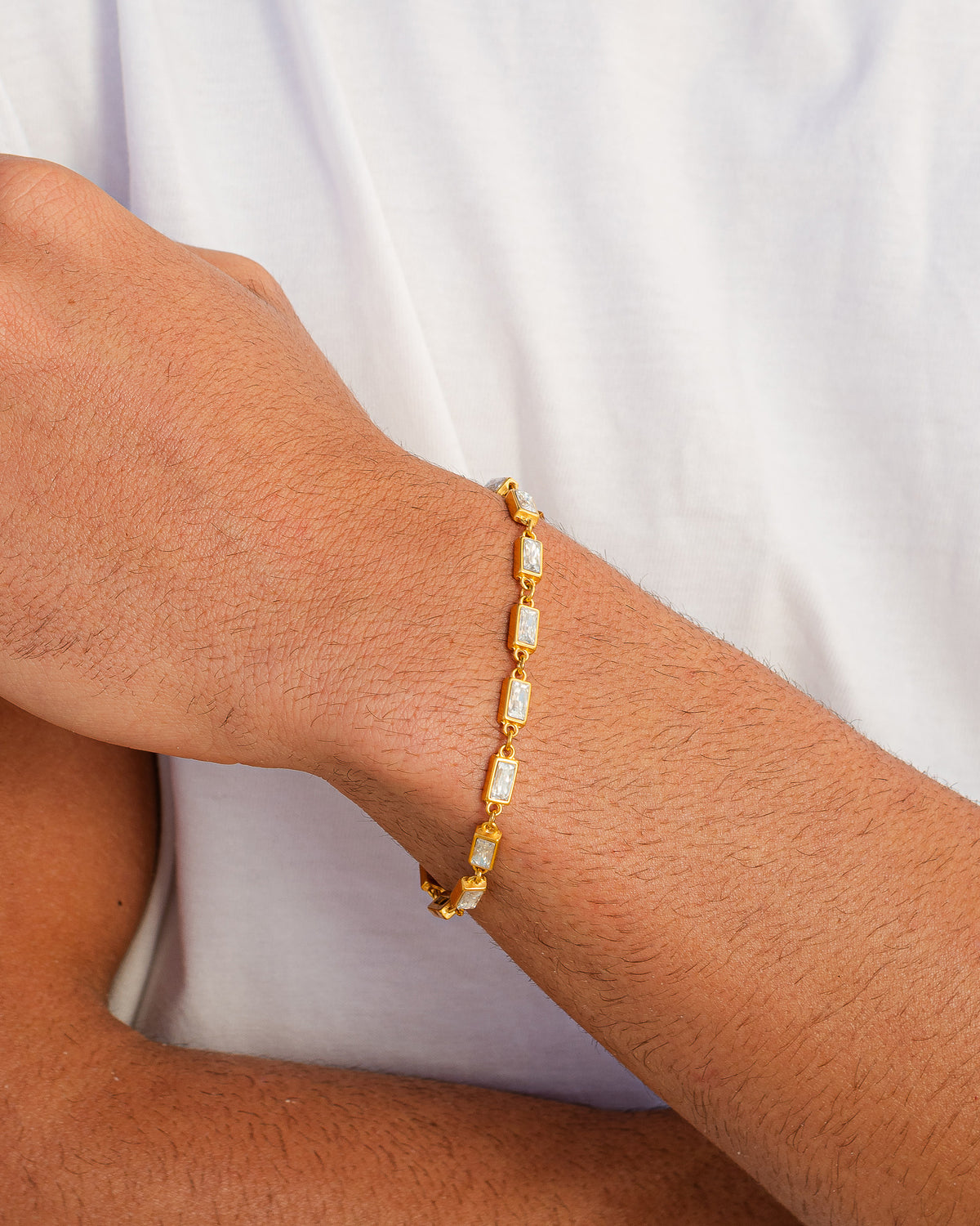 Pulsera OMEN GOLD con piedras cuadradas transparentes sobre una cadena de oro fina en la muñeca
