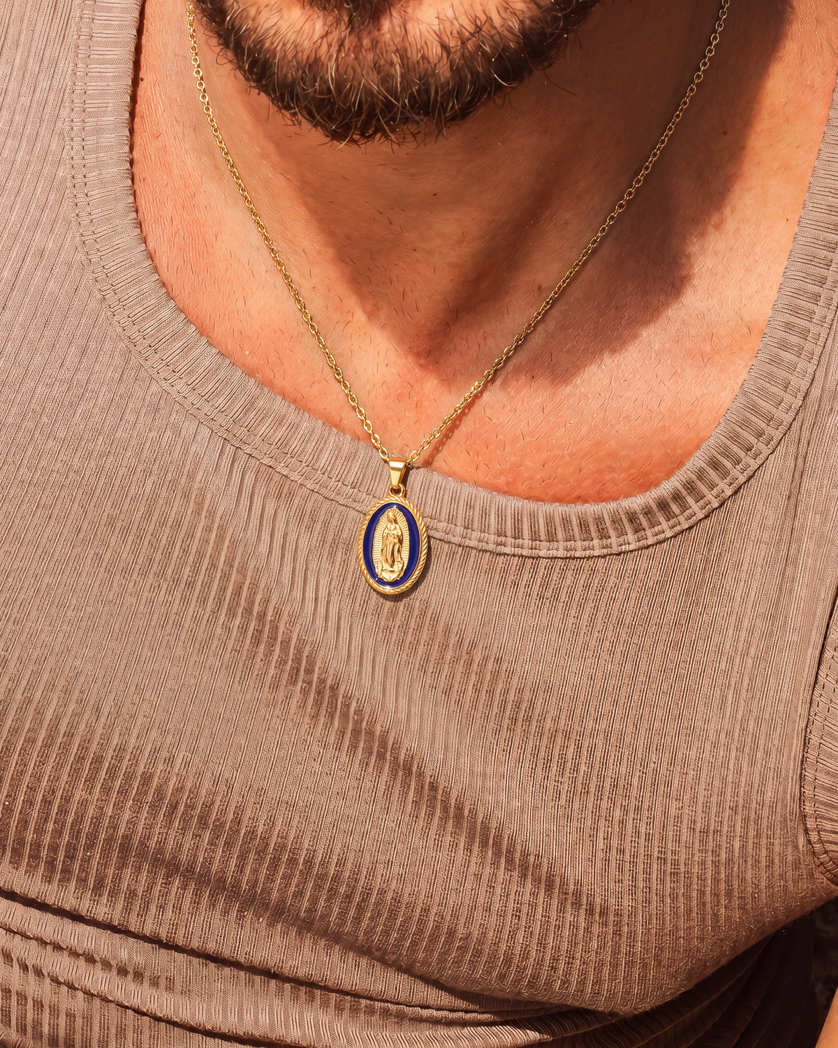 Gold Virgin Mary necklace worn on a taupe knit top with blue enamel oval pendant