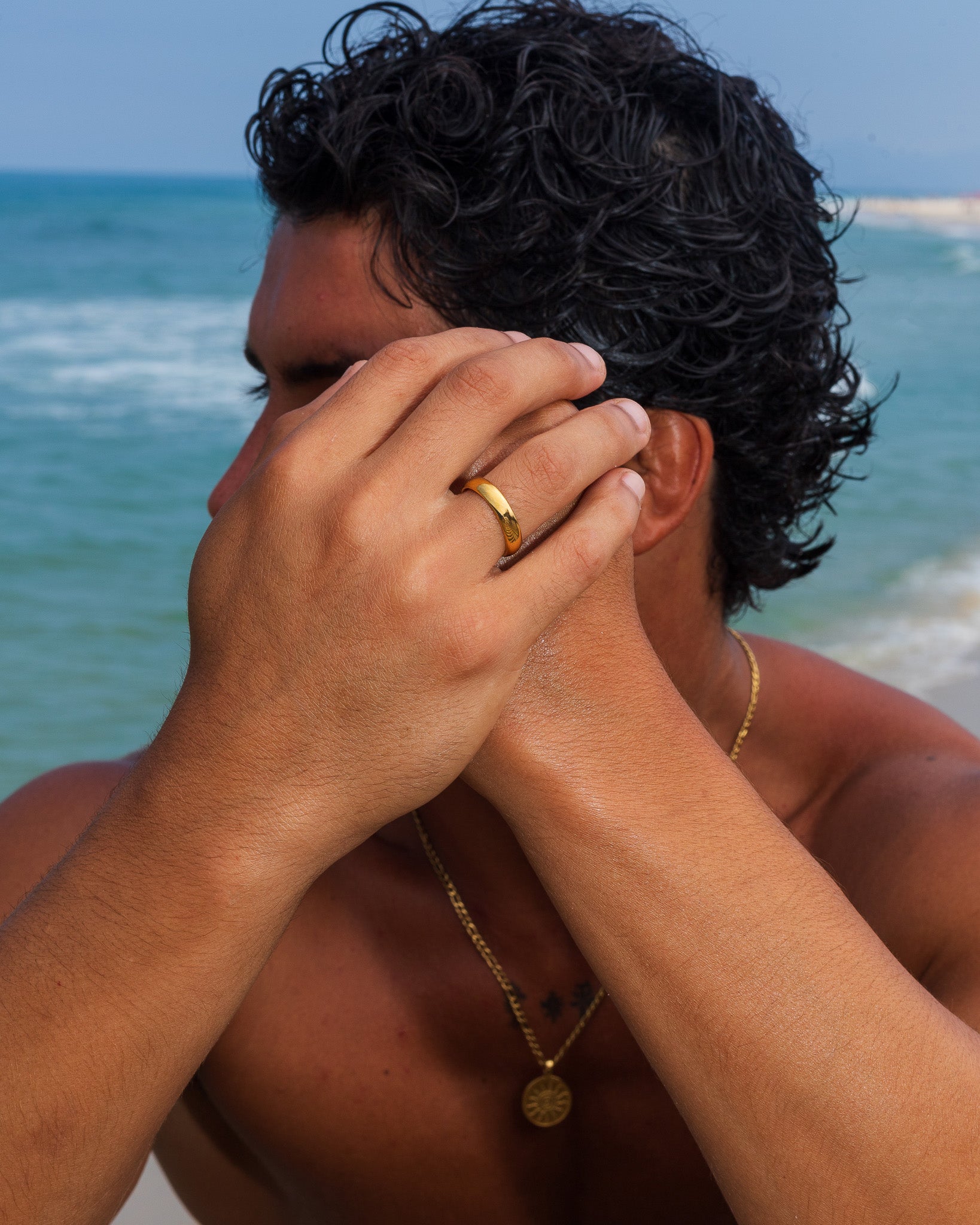 Anillo de oro liso en un dedo, cerca de la cabeza, con el mar de fondo