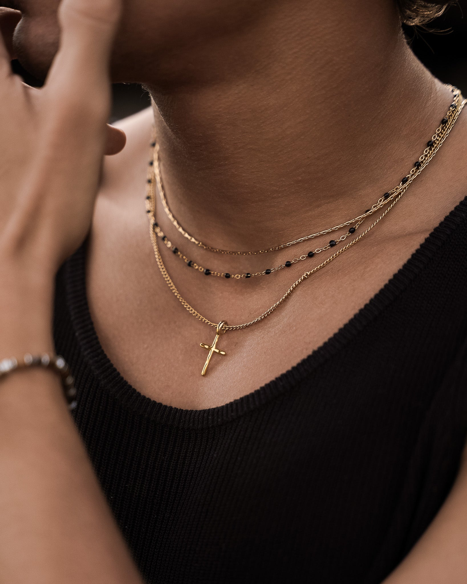 Gold cross pendant necklace layered with delicate chains on a model's chest