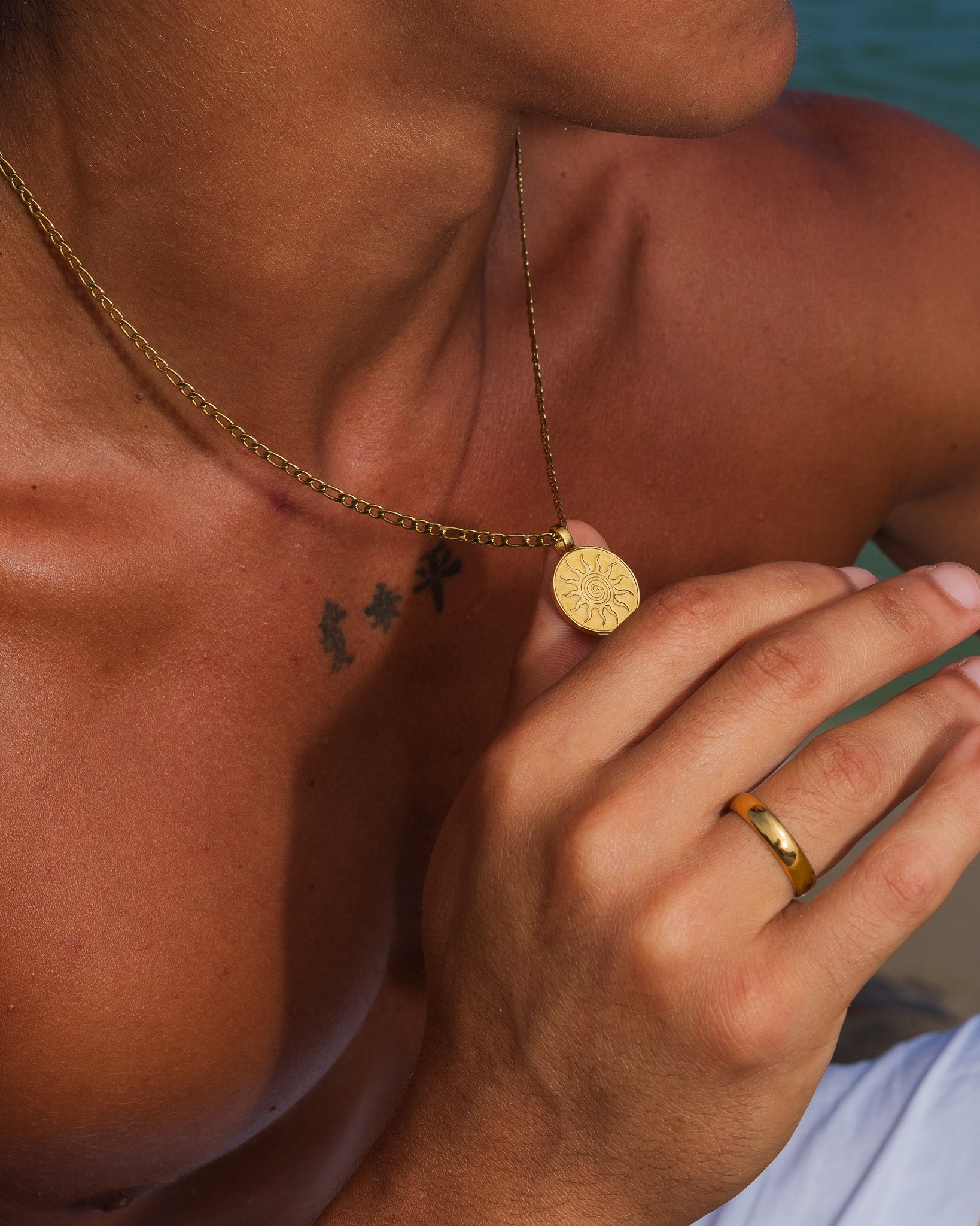 Collar ENERGY de oro con colgante redondo de sol radiante sobre un pecho bronceado.