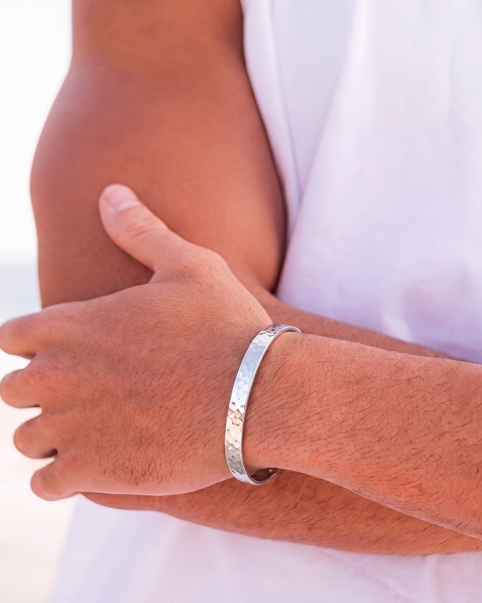 Hammered silver bracelet on a man's wrist wearing a white shirt