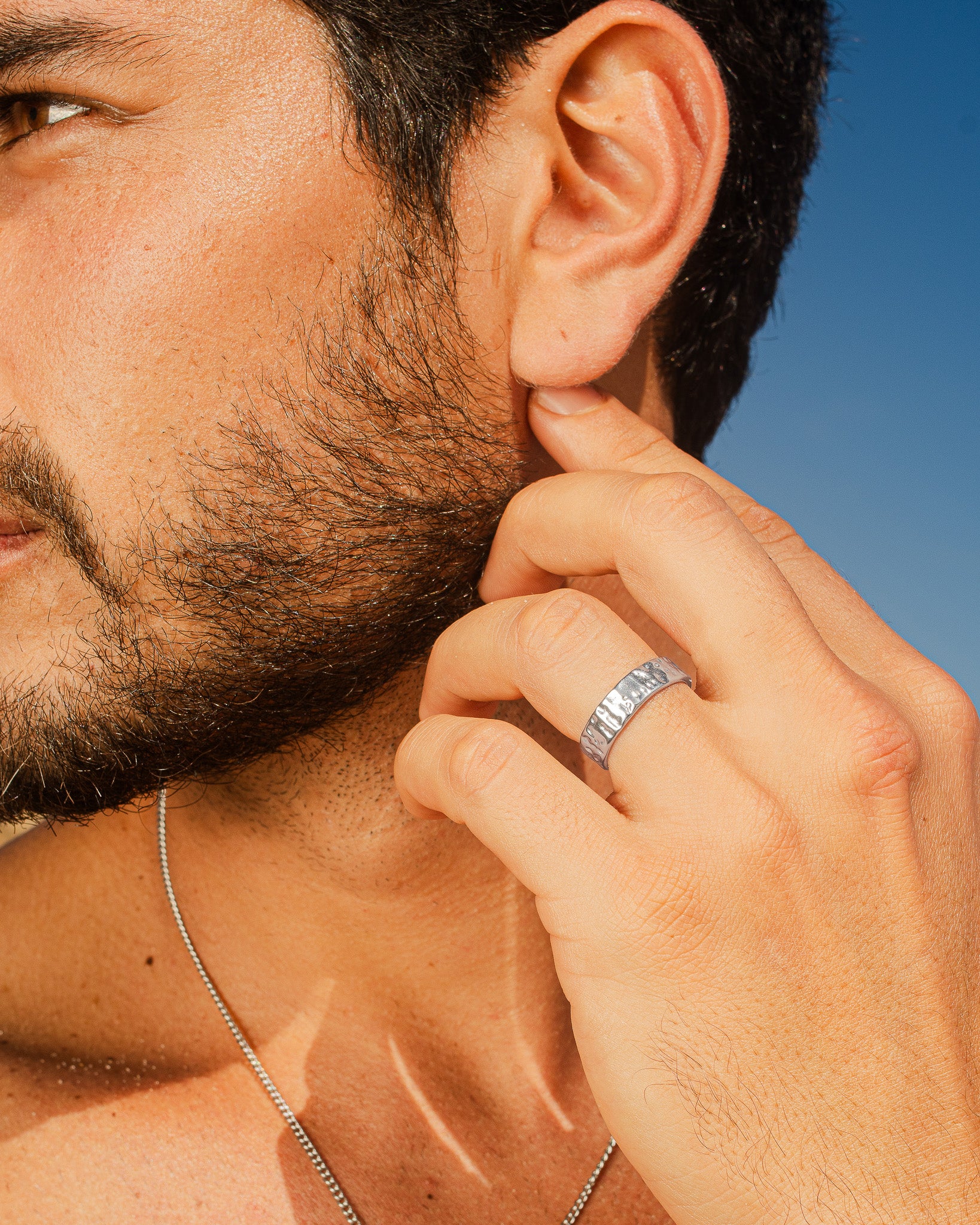 Profile of a man wearing the hammered silver 6mm ring on his finger with a silver chain necklace visible at the neck.