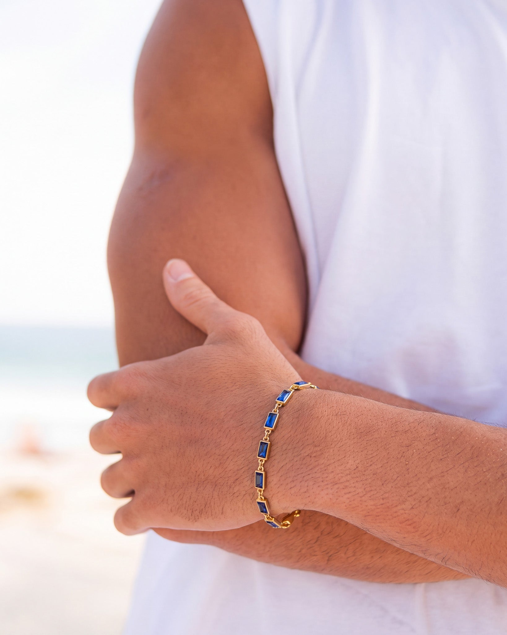 Vista parcial de la pulsera OMEN de oro con piedras azules en un brazo, junto a una camisa blanca.